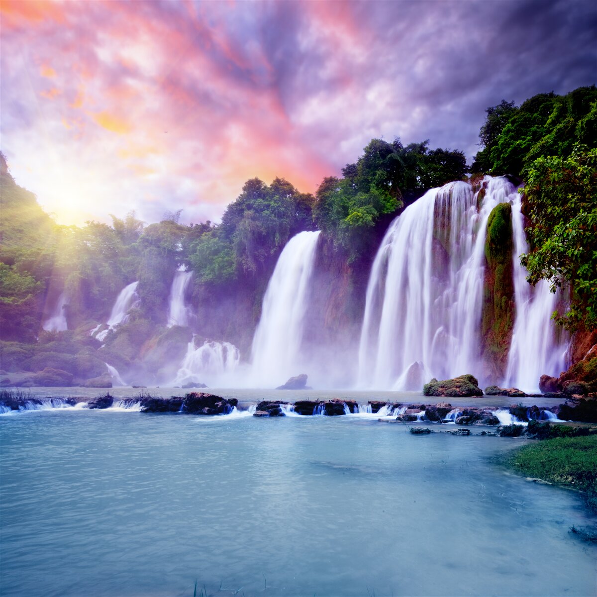 Fototapeten Ein riesiger Wasserfall fällt mit einer Kaskade vor dem Hintergrund der untergehenden Sonne